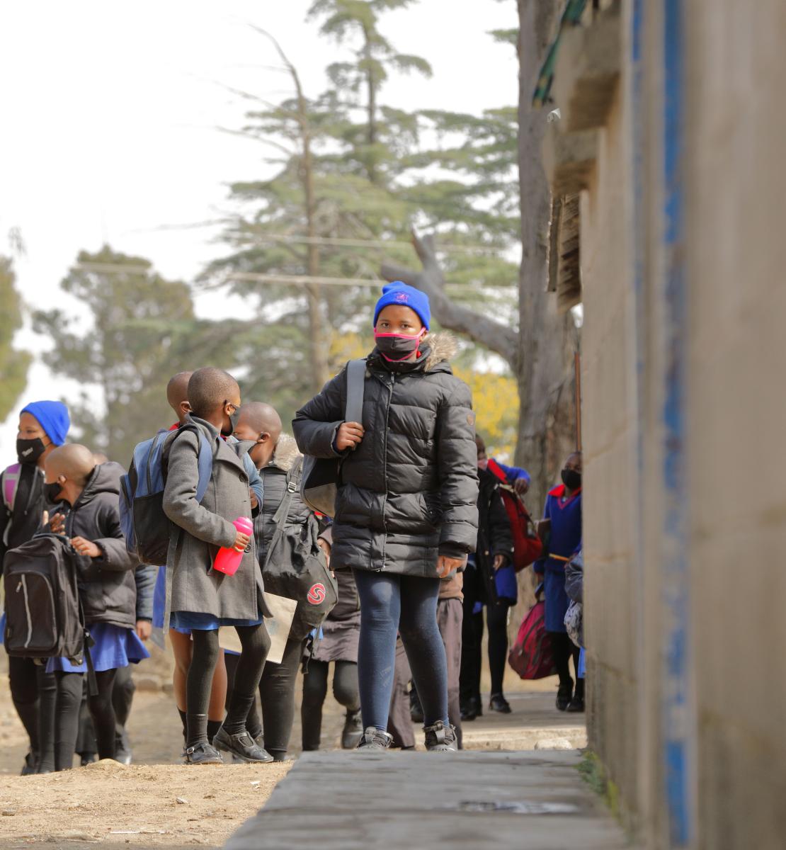 Группа детей школьного возраста в масках на лицах выходят из здания школы. 