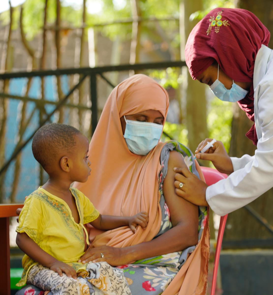 A woman with a child on her lap is vaccinated by a health professional. 