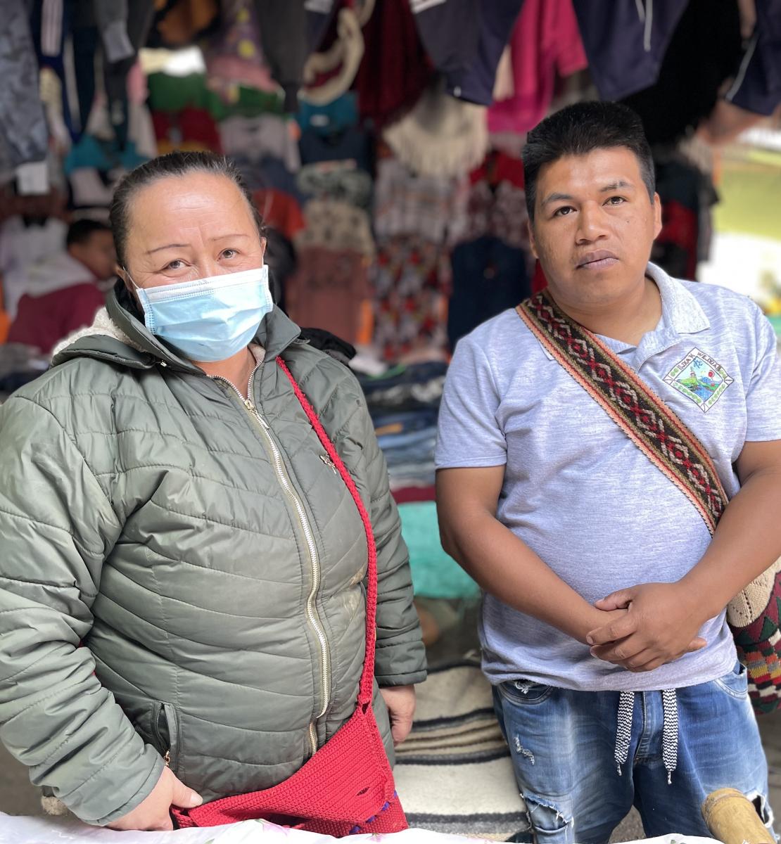 Una mujer con mascarilla y un hombre se encuentran uno al lado del otro en un mercado callejero.