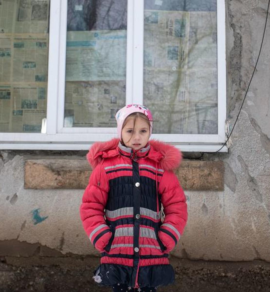 6 февраля 2022 года. Девятилетняя девочка стоит перед разрушенным в результате конфликта фасадом своего дома на востоке Украины.