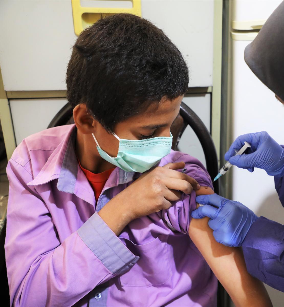 Un pequeño con mascarilla recibe una vacuna contra la COVID-19 en un asentamiento en Saveh, Teherán.