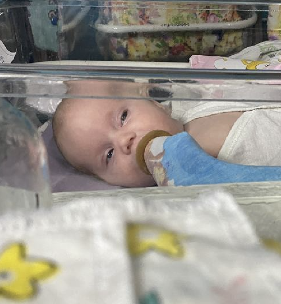 一个婴儿躺在一个塑料摇篮里，嘴里插着一根氧气管。