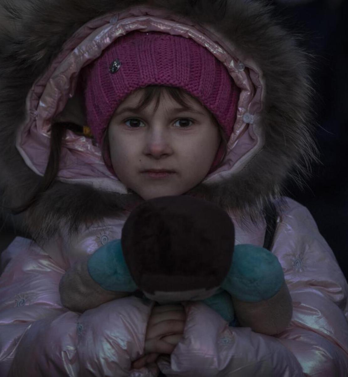 Une petite fille est emmitouflée dans un gros manteau rose et tient un ours en peluche dans les mains.