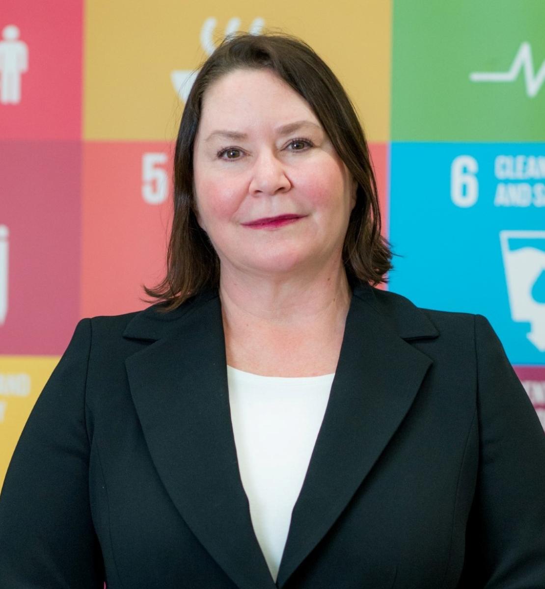 A woman stands in front of a sign with SDG logos on it. 