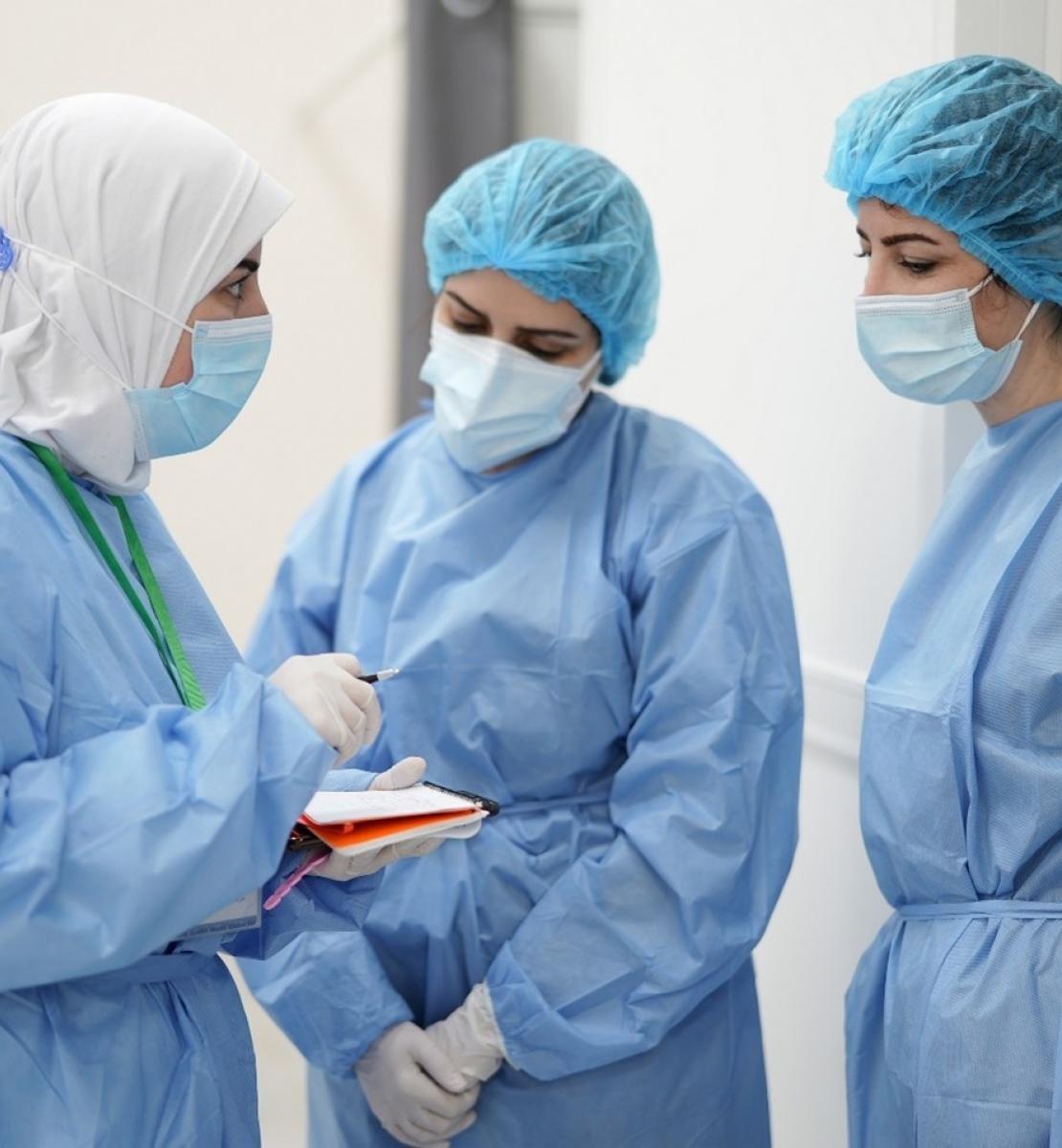 Three medical professionals huddle together, all wearing scrubs. 