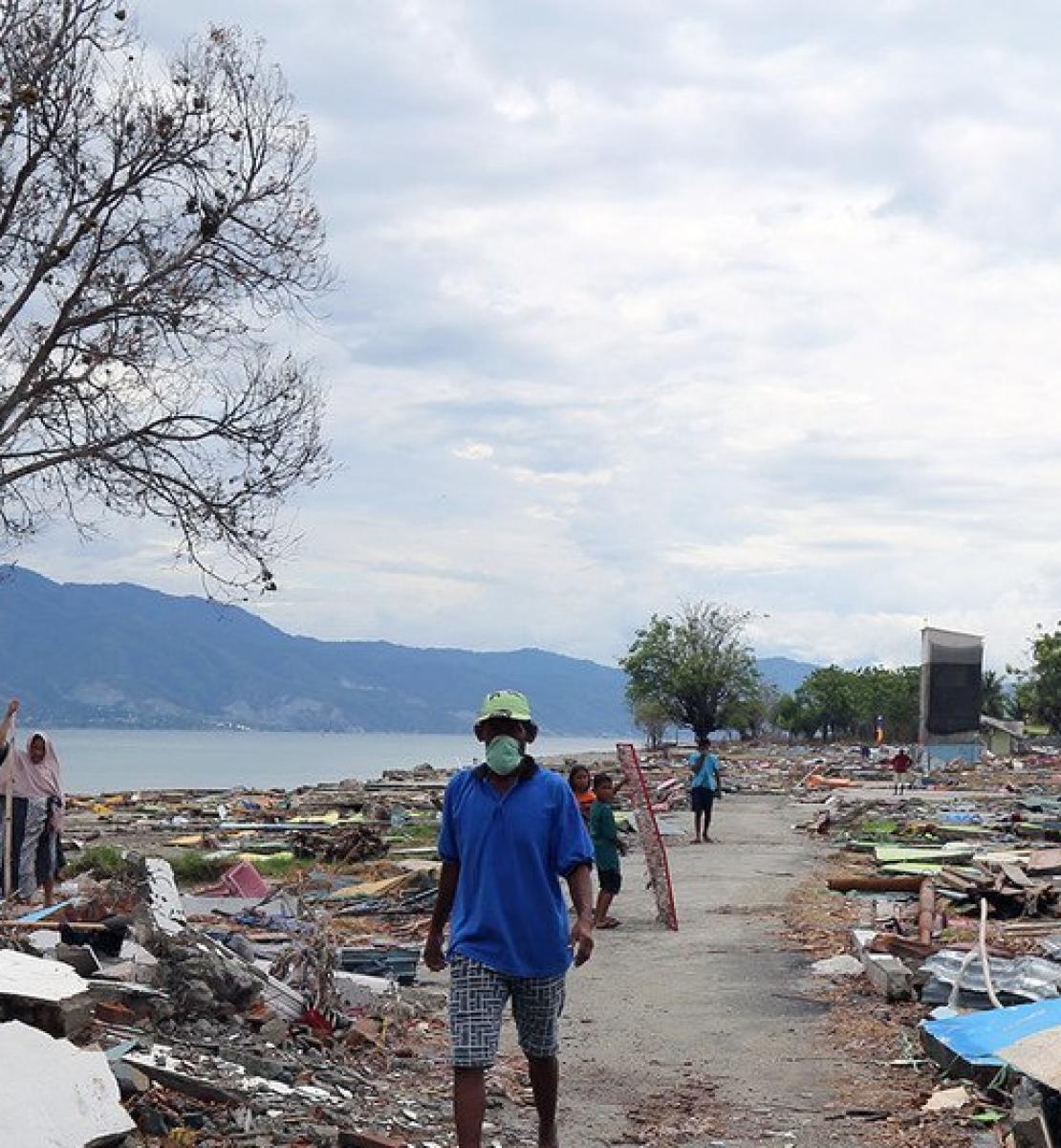 A man scours debris and building remnants on a waterfront.