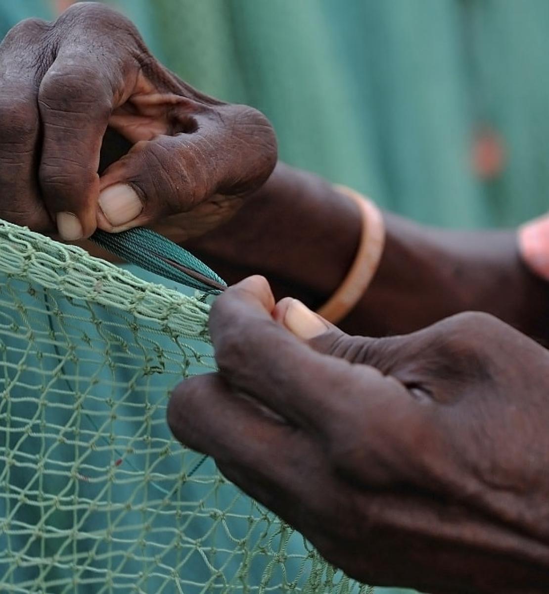 A close-up photo of a woman's hands weaving a fisher's net.
