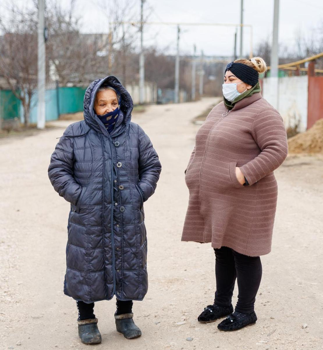 Две женщины в зимних пальто разговаривают на улице. 