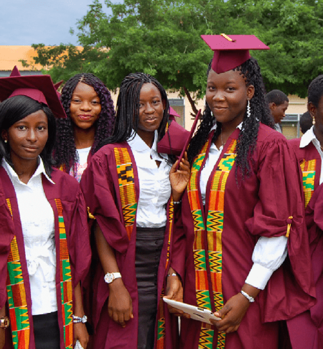 Plusieurs jeunes filles vêtues d'une tenue de diplômées de couleur violette se tiennent devant la caméra en souriant fièrement. 