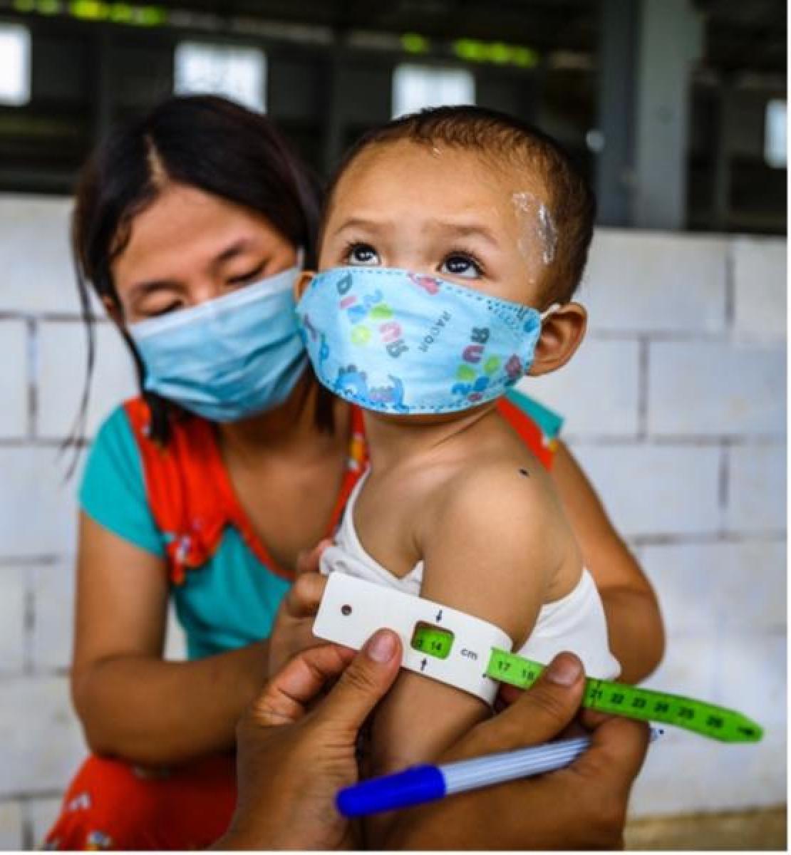Au Myanmar, une infirmière administre un vaccin à un jeune enfant rohingya tandis que sa mère le tient sur ses genoux.