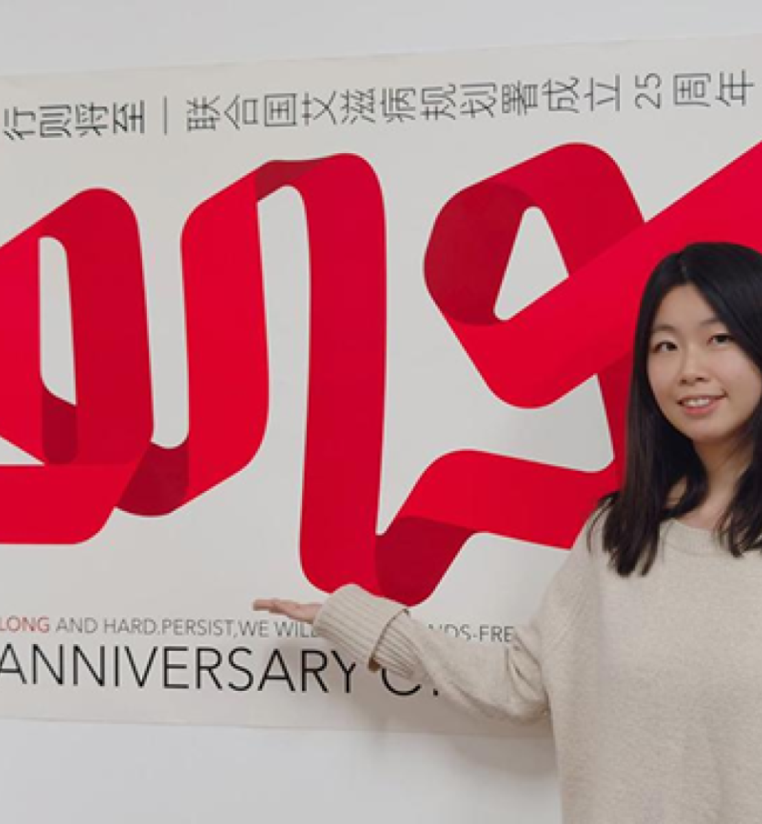 一位年轻的中国妇女站在红丝带的海报前。