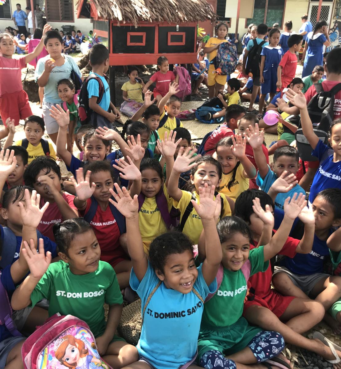 Niños y niñas con ropas de colores levantando las manos al aire.