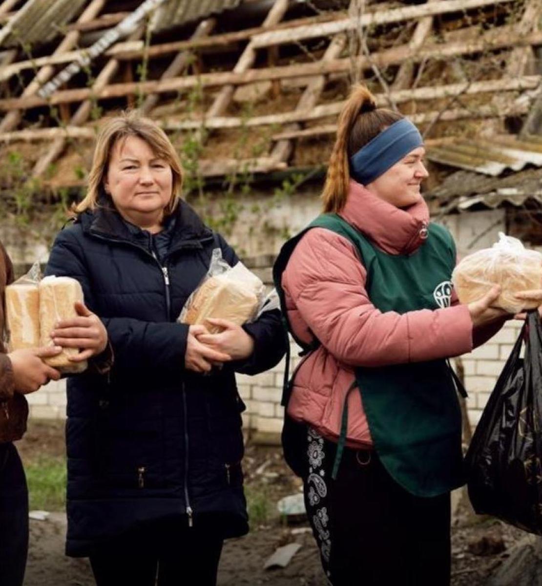волонтер раздает женщинам буханки хлеба.