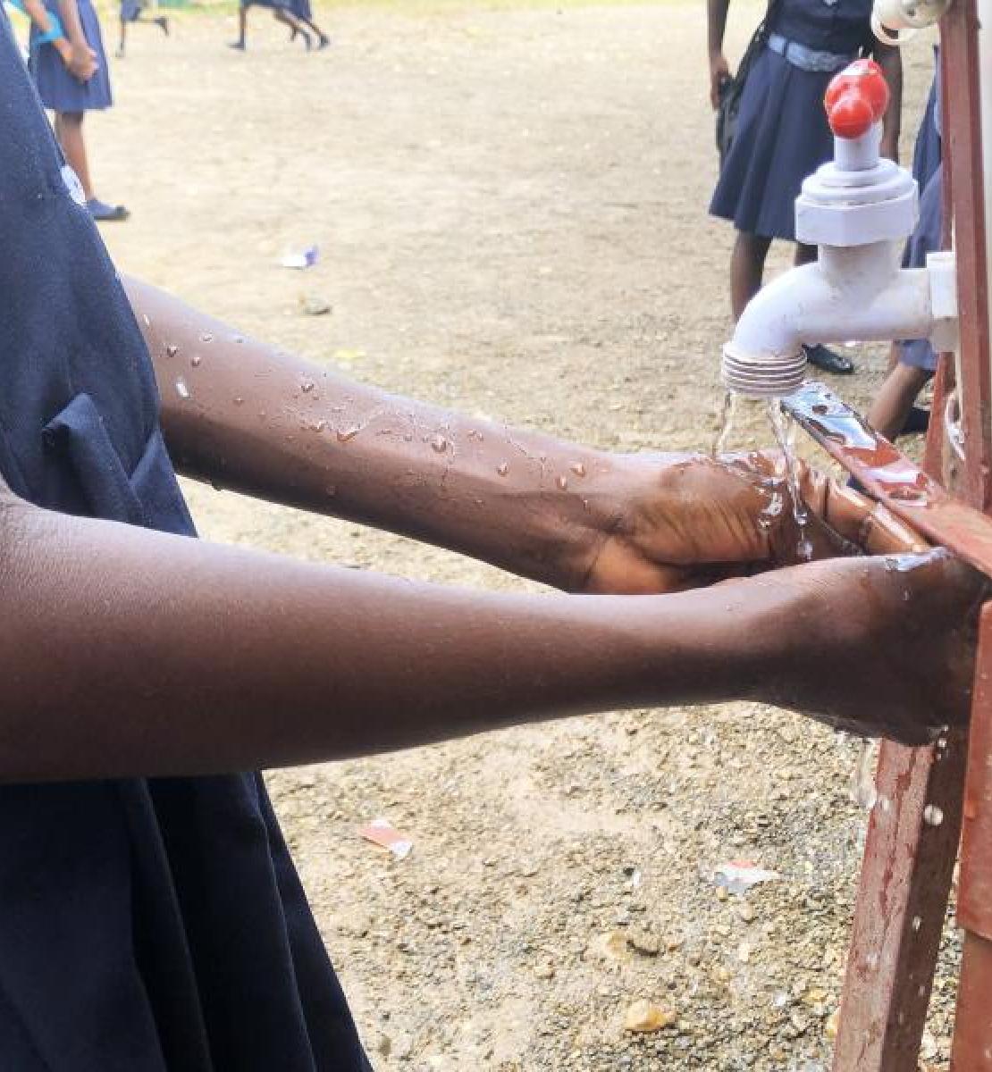 A girl in what seems to be a dark-blue school uniform washes her hands with soap outside.