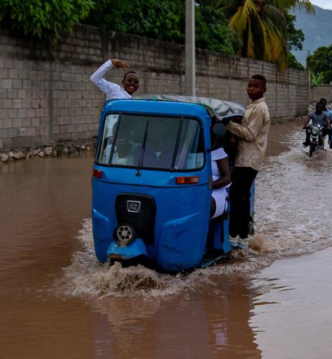 Two boys standing inside a motor vehicle that is stuck in the middle of a flood