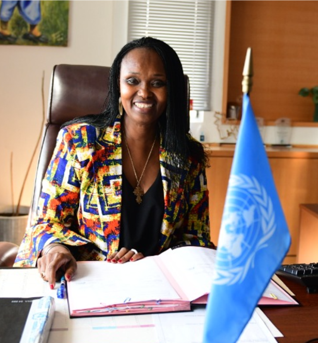 Femme dans une chemise colorée assise à un bureau avec un drapeau de l'ONU