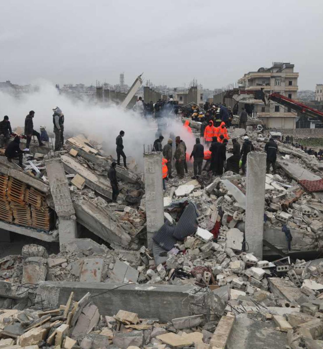Several people standing on debris from building destroyed by earthquake in Syria