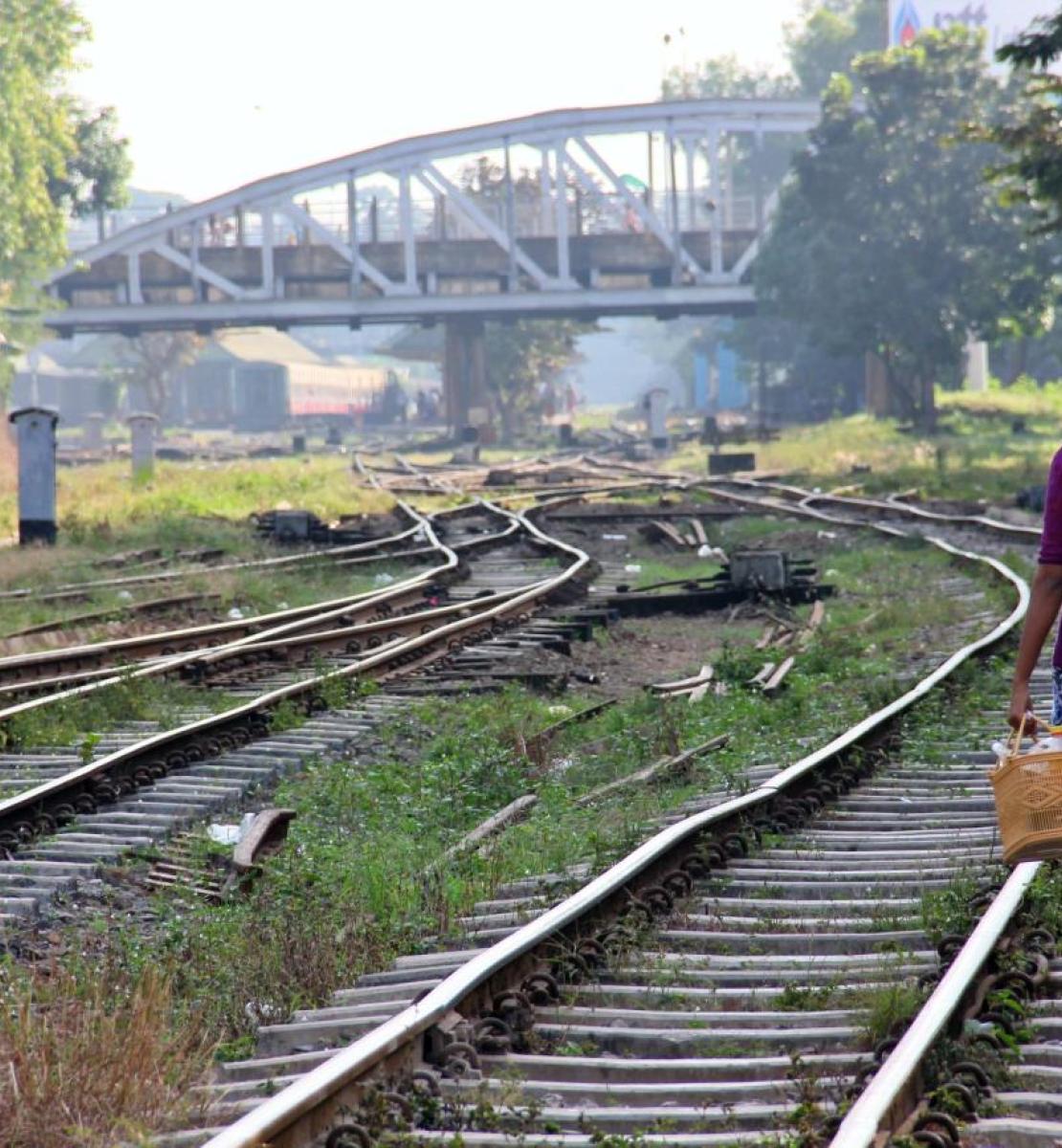 A woman in a purple top walks along a railroad on a sunny day. 