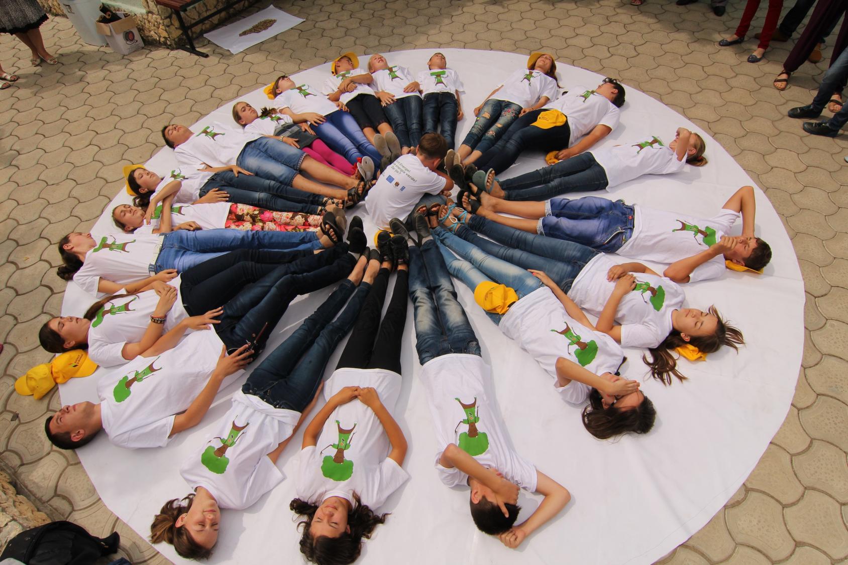 Jóvenes acostados formando un círculo sobre una tela blanca circular.