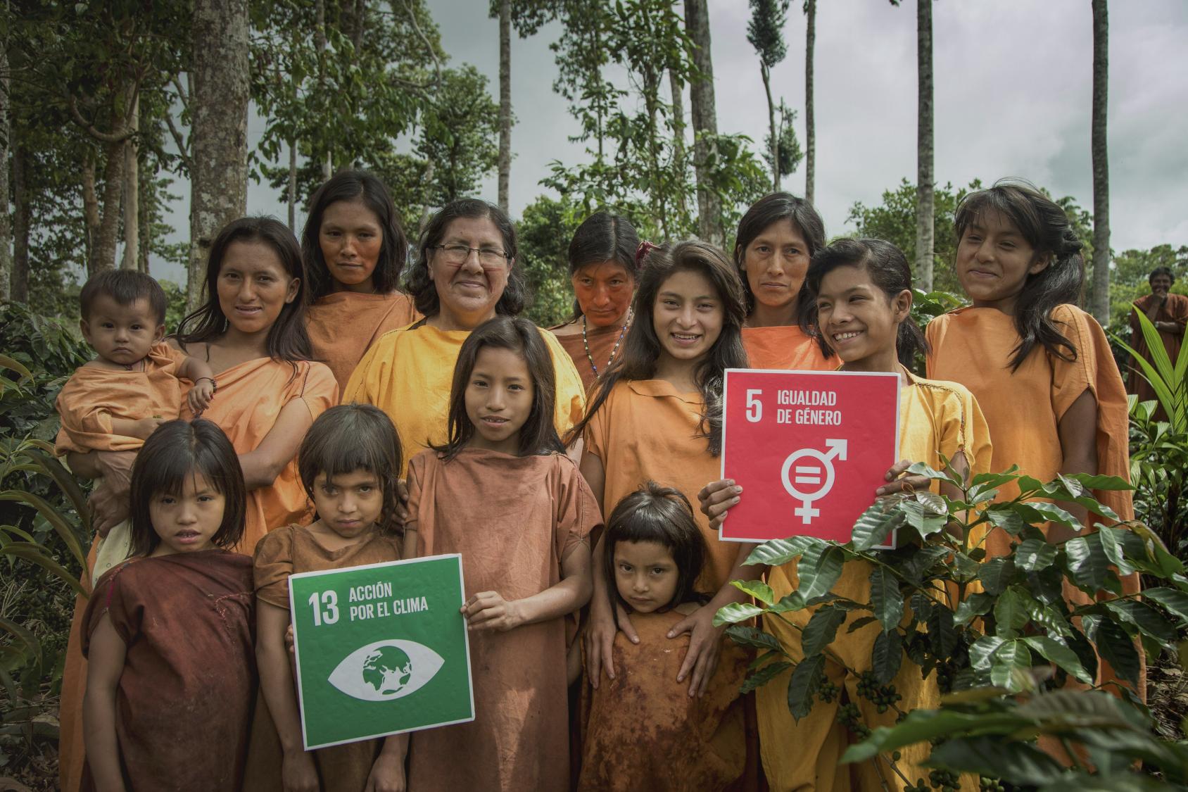 A group of indigenous women and girls smile as they hold signs for SDG 5 and 13. 