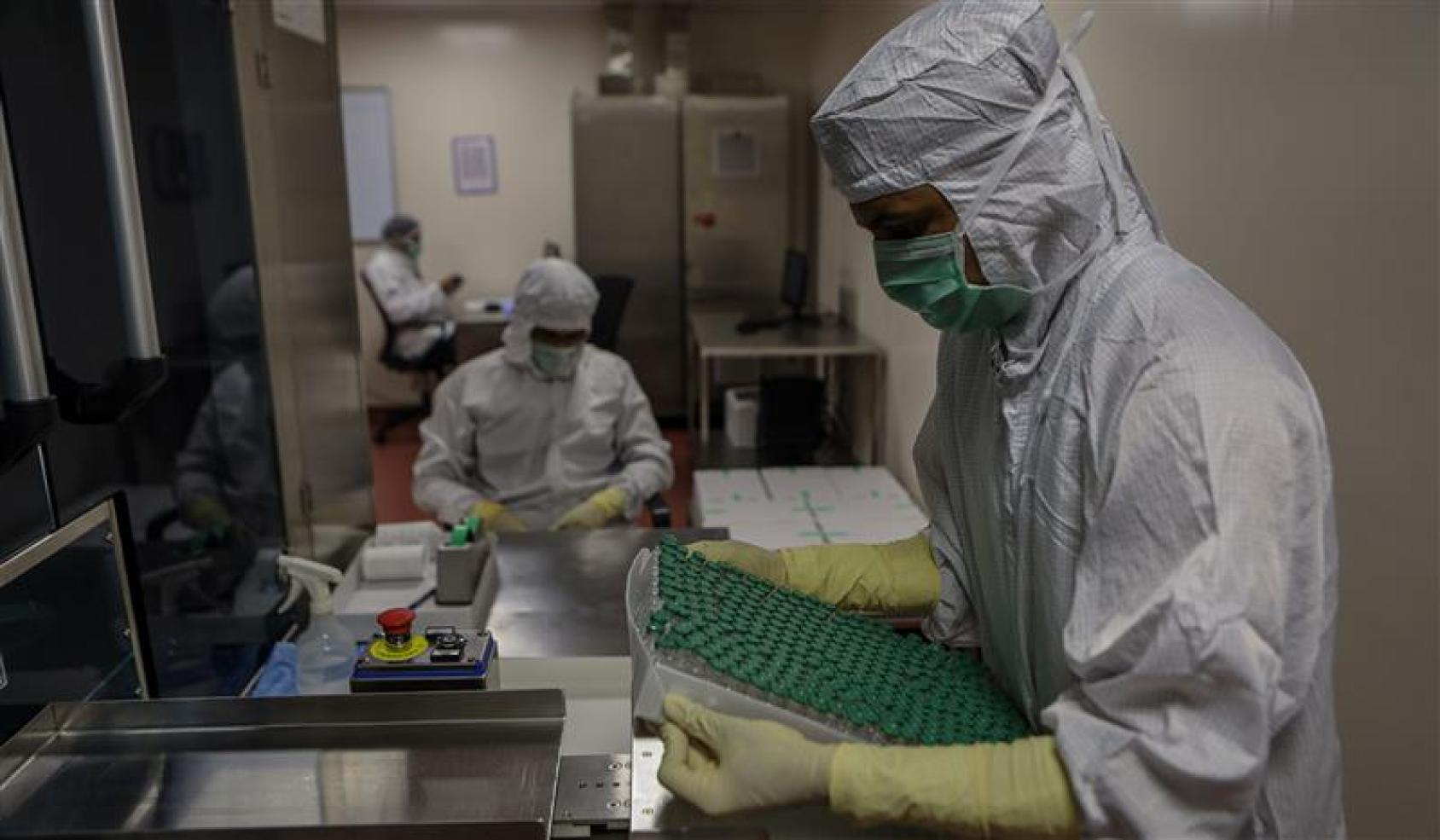 Two people with full protective gear prepare COVAX vaccines in an office. 
