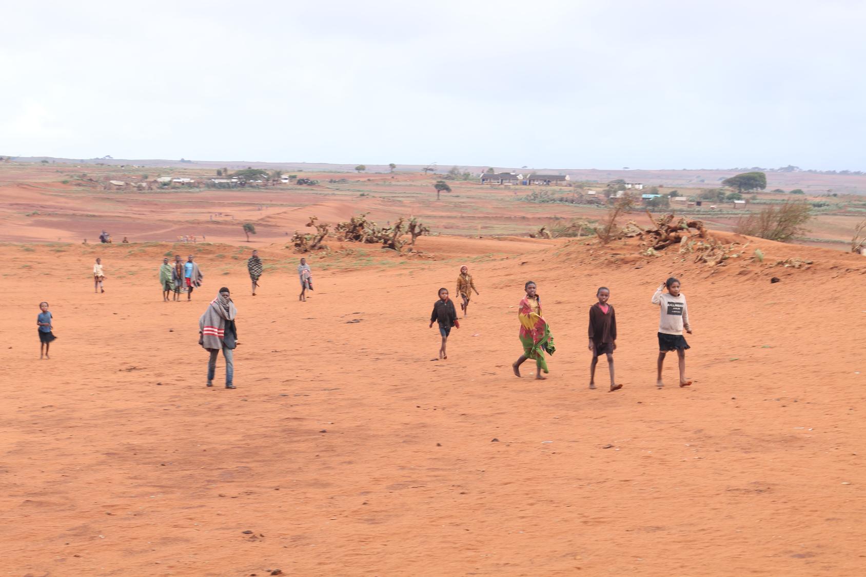 Several people walk over agricultural land covered by sand. 