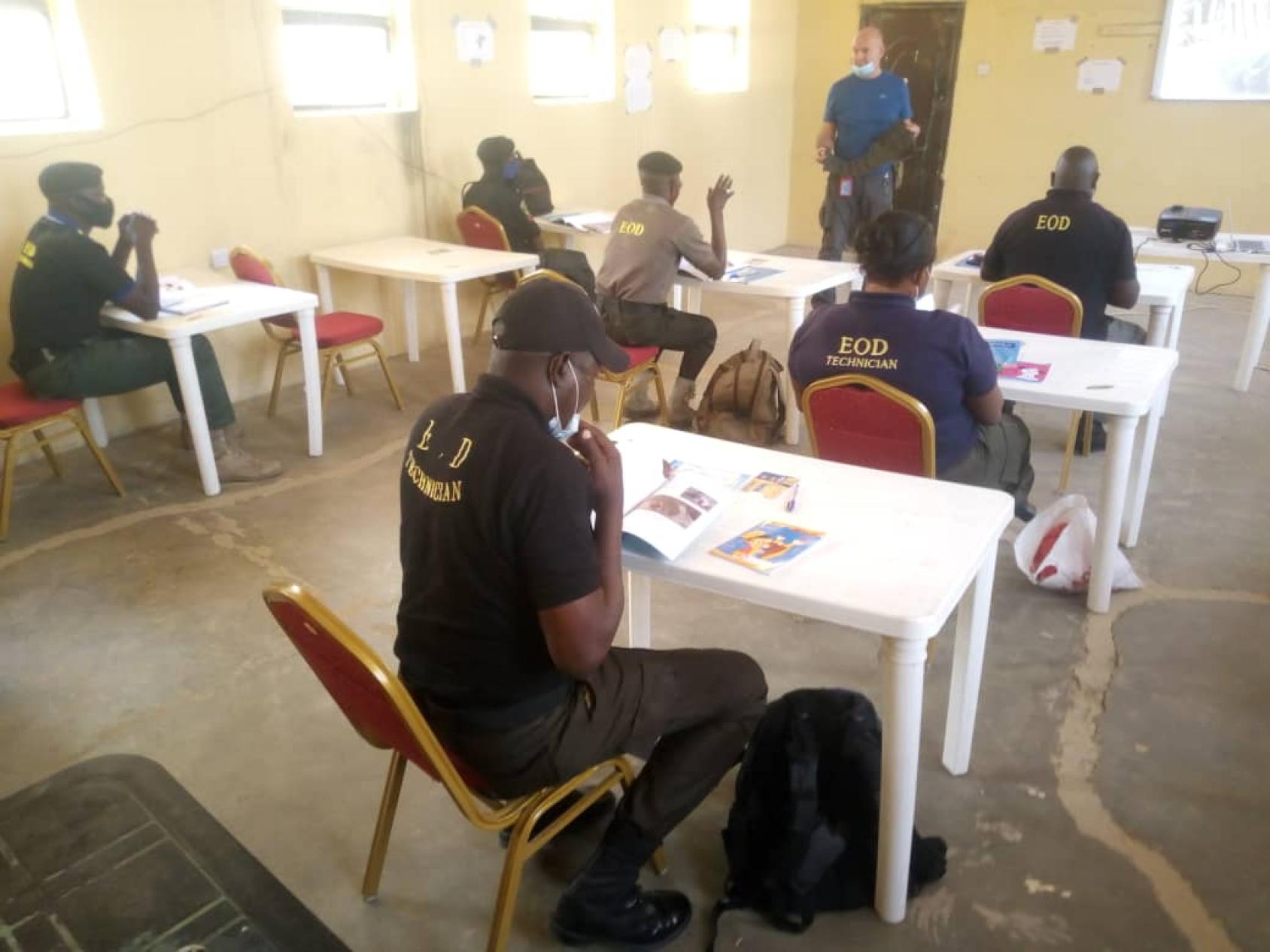 National security officers sit in socially distanced desks in a classroom.