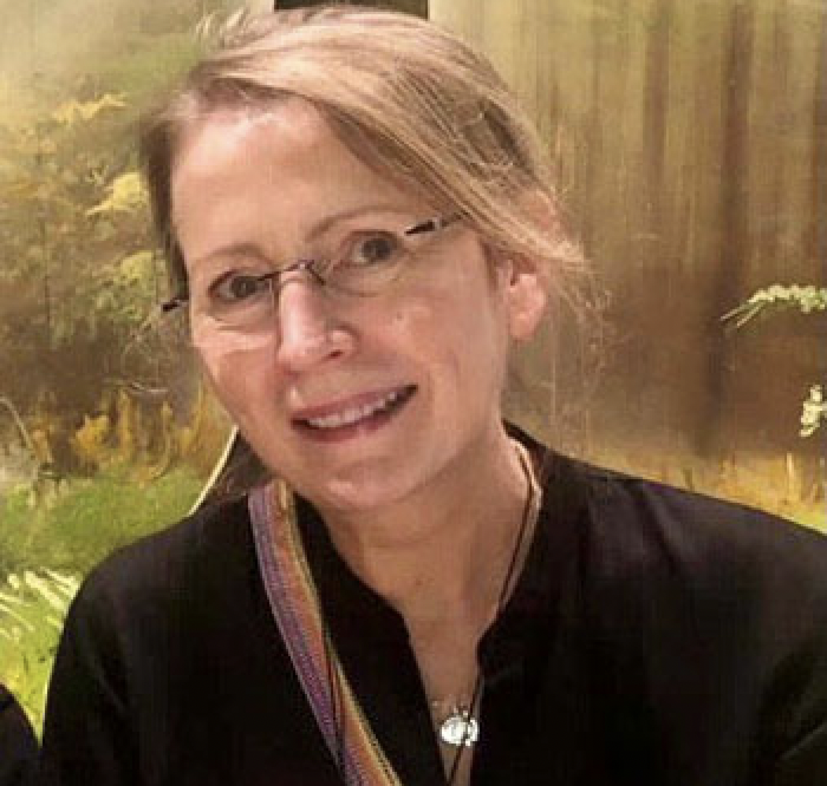 A woman with glasses and a black shirt smiles at the camera. 