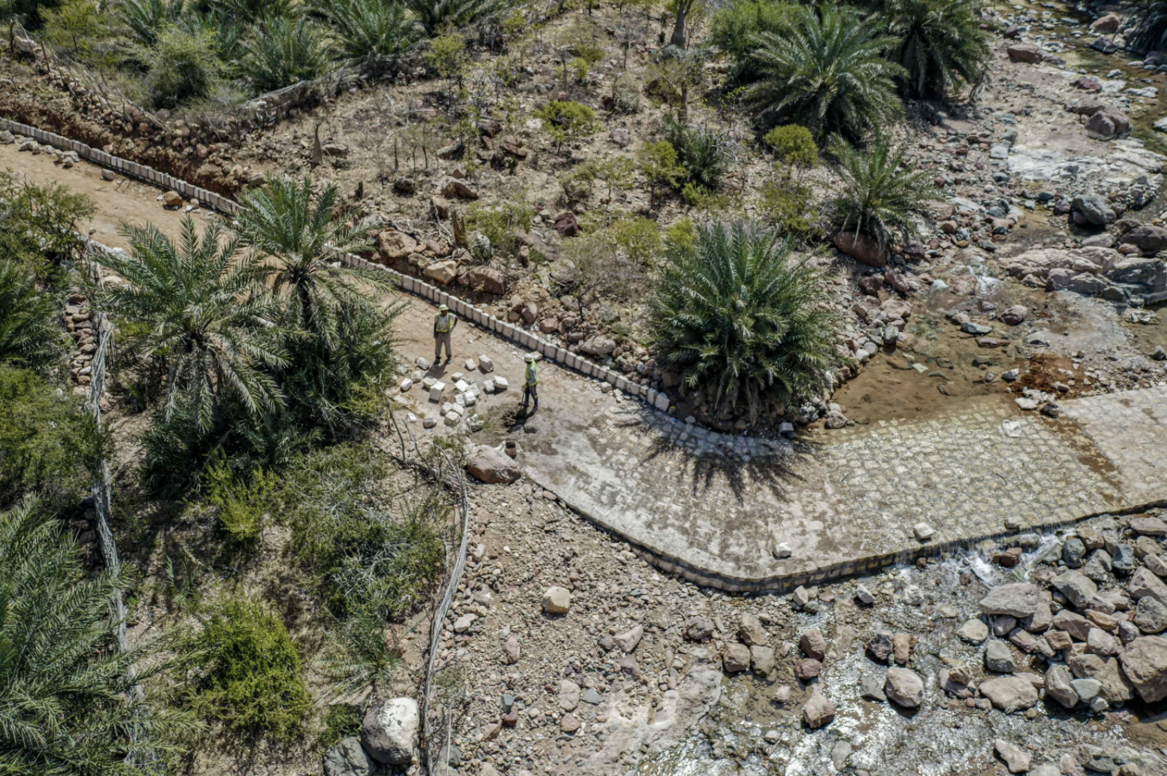 Image aérienne d'une route en cours de réparation au milieu d'une terre sur laquelle poussent des palmiers.