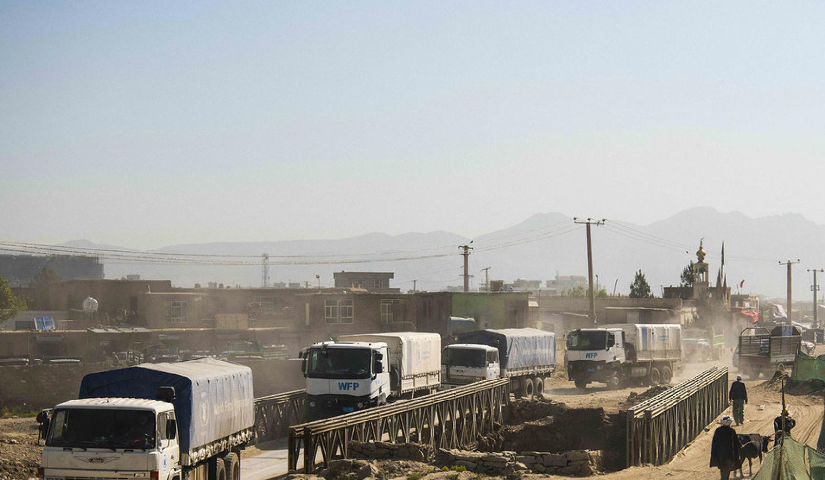 A line of WFP trucks drive through a dusty road delivering essential food supplies. 