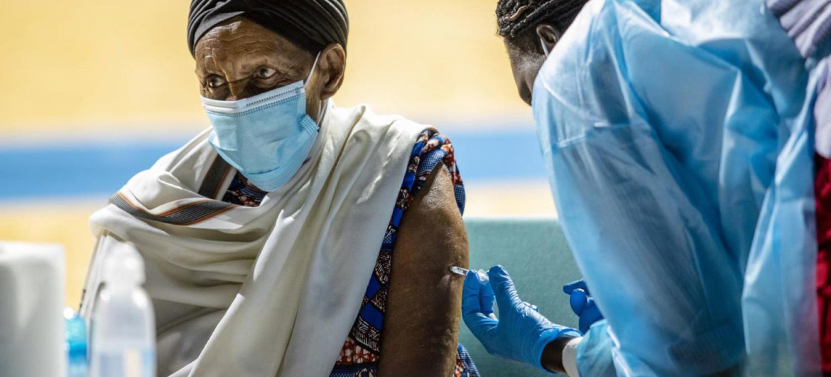 Un homme portant un masque chirurgical se fait vacciner contre la COVID-19 par un membre du personnel de santé.