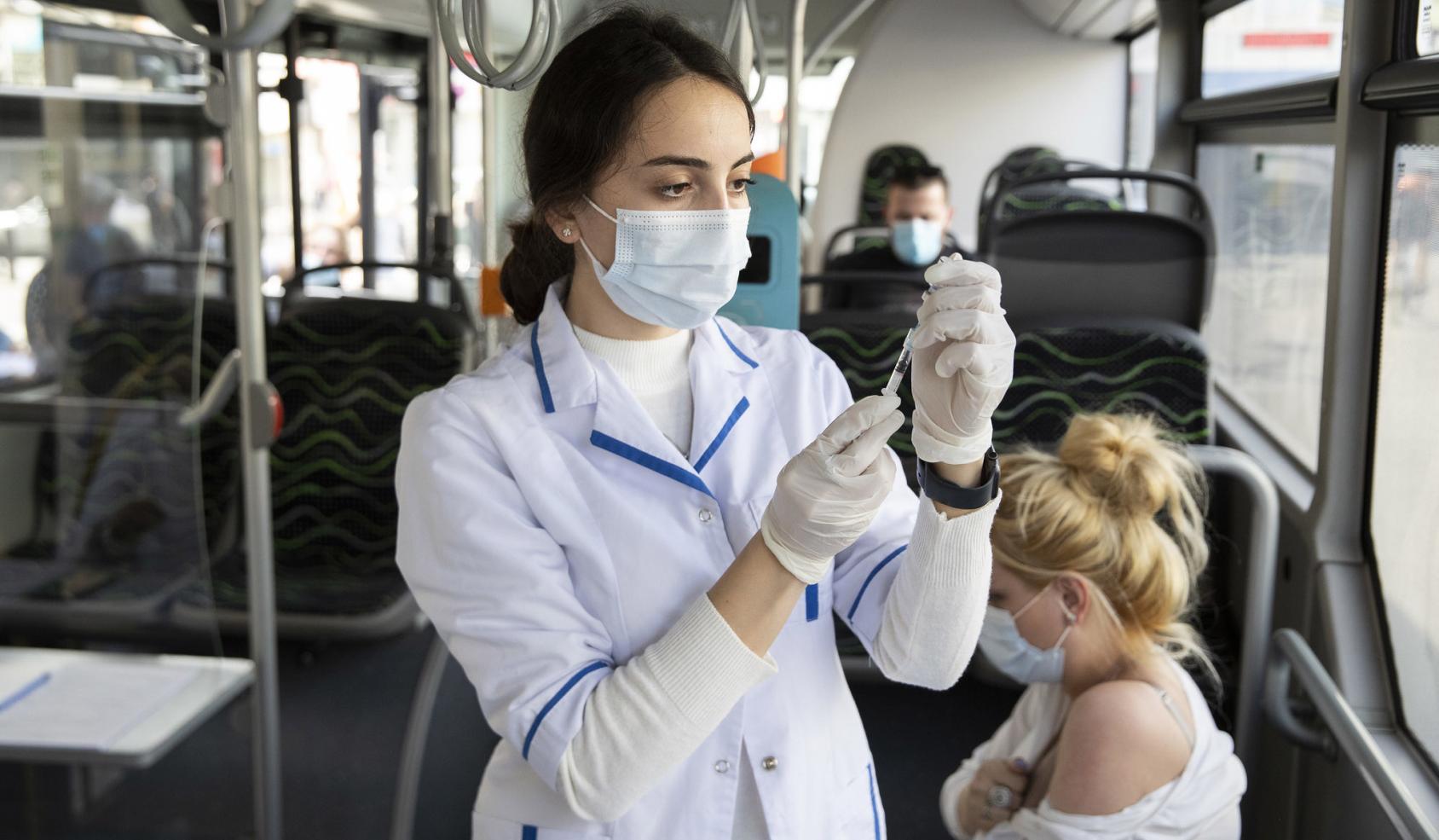 A healthcare worker prepares a COVID-19 vaccine for a patient on a dedicated vaccine bus.