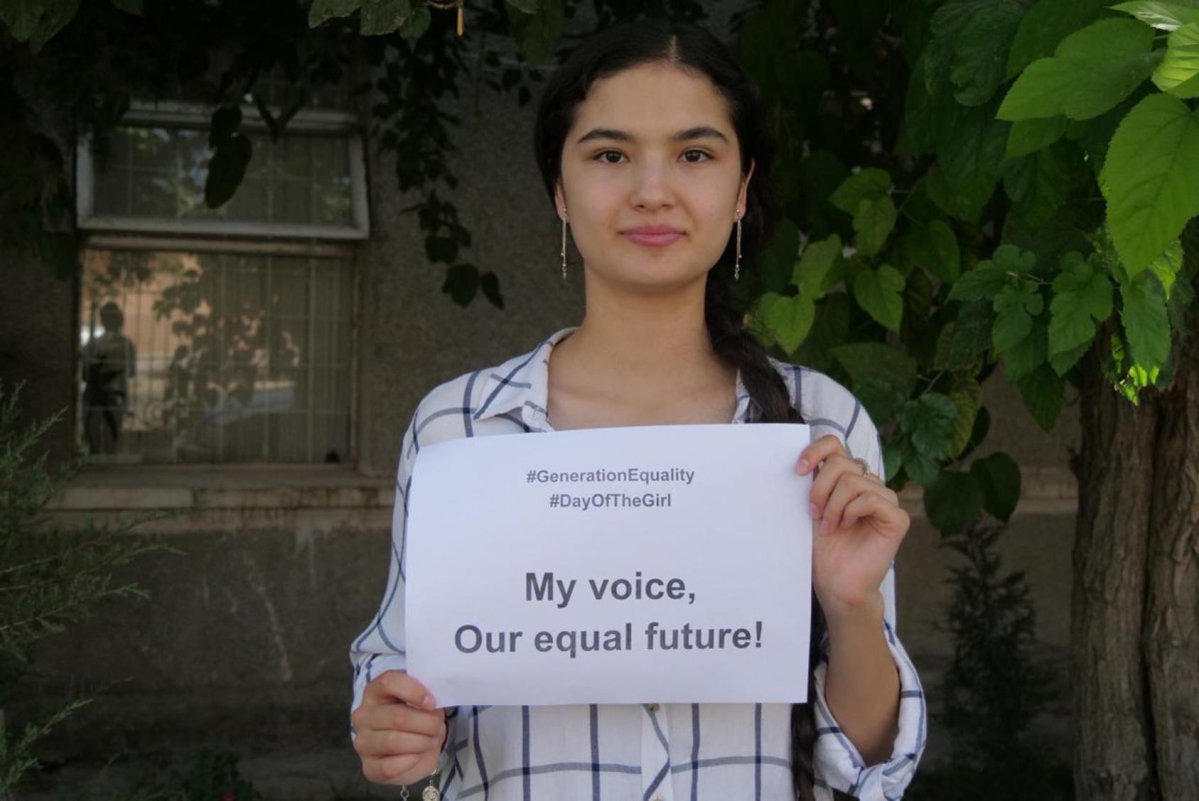 A girl holds a sign that says "My voice our equal future!" in English. 