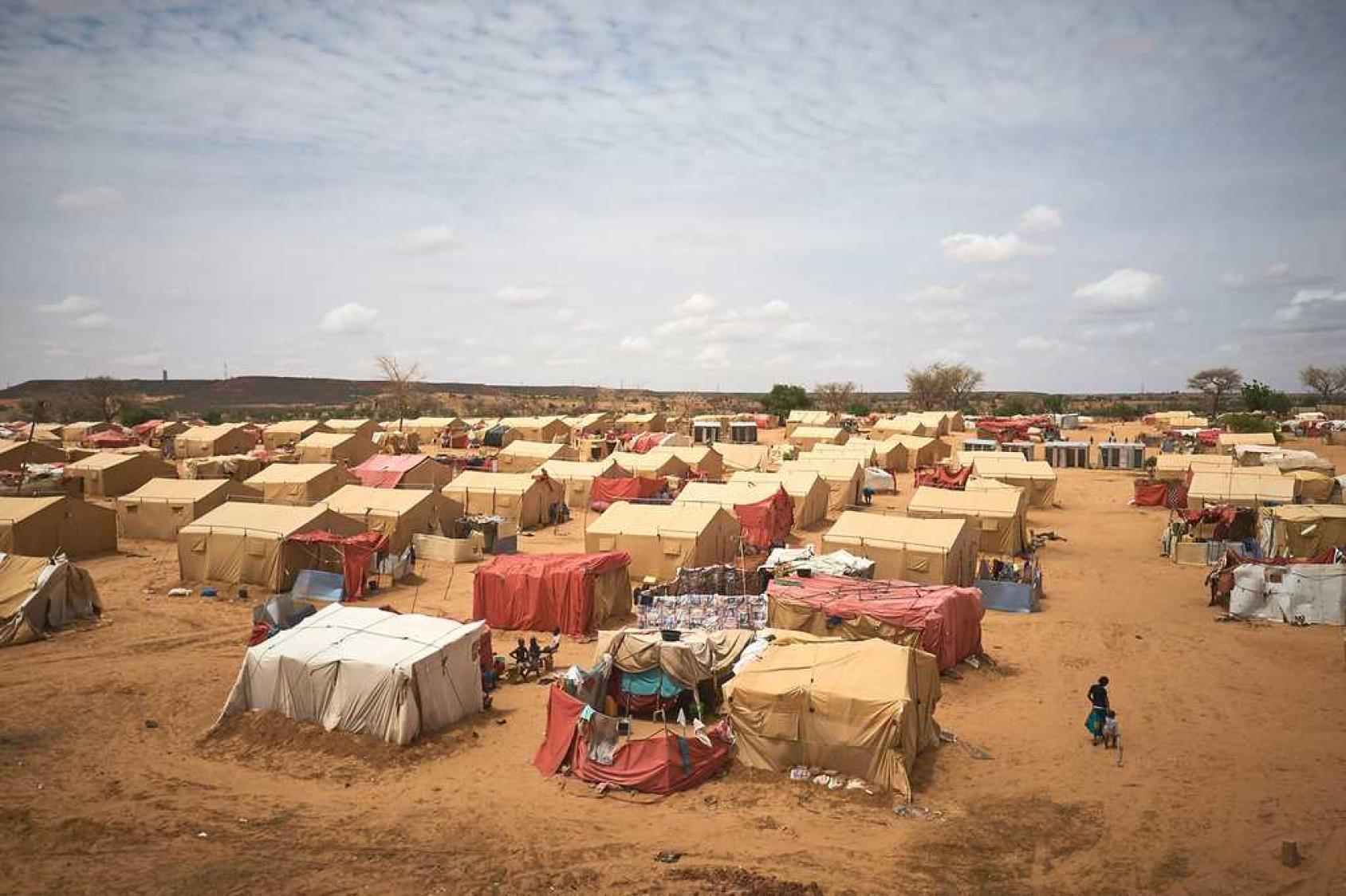 Vue d'un campement où plusieurs personnes s'affairent autour des tentes qui leurs servent d'abri, au milieu d'une étendue désertique.