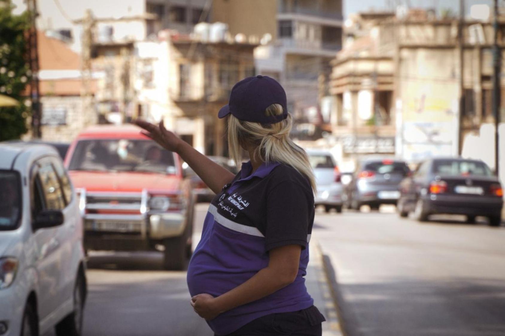 A heavily pregnant woman directs traffic in the street. 