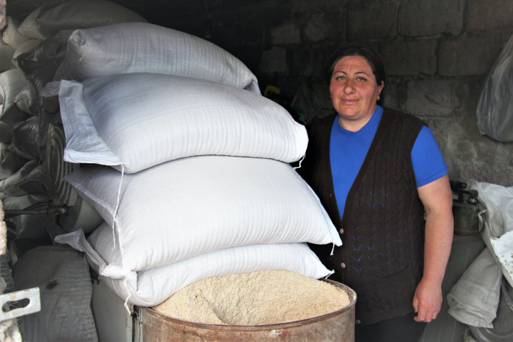A woman stands next to a large pile of white sacks. 