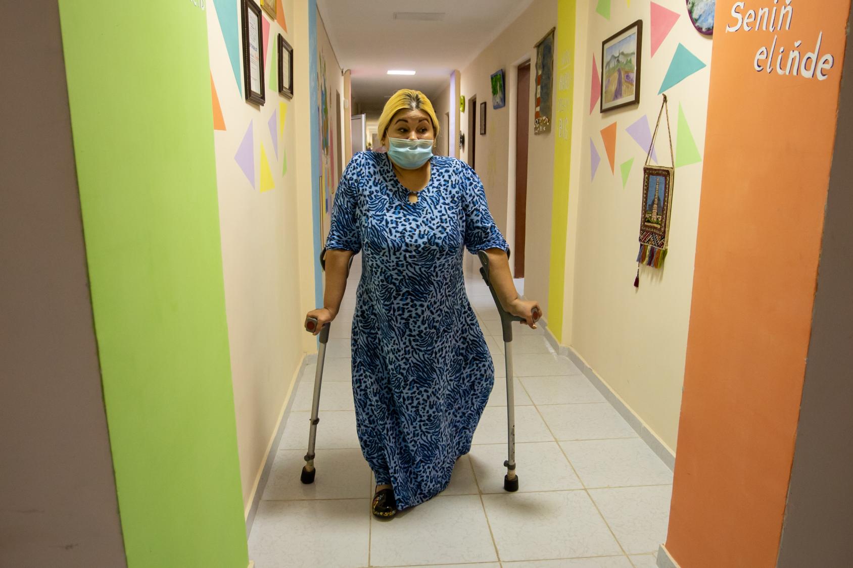 A woman walks down a colorful hallway with crutches.