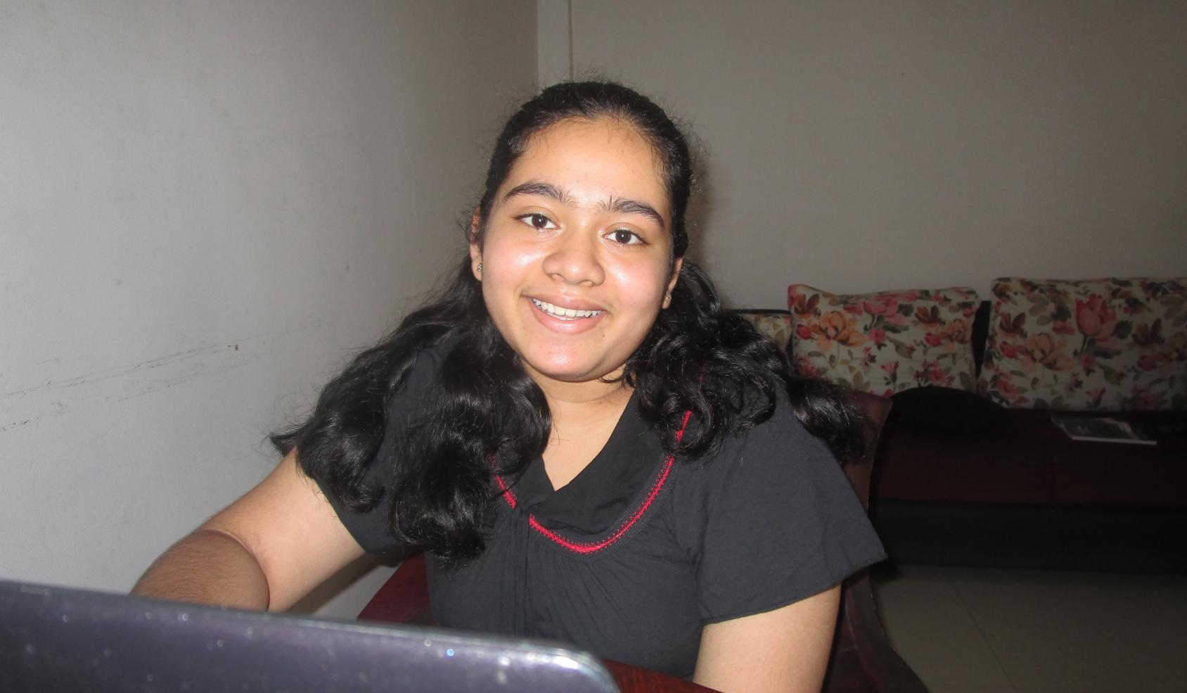 An adolescent girl sits at her computer and smiles at the camera.