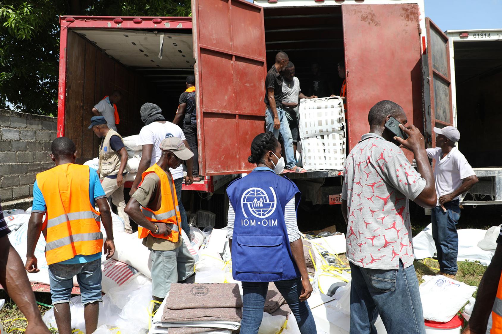 Several people work together to unload humanitarian aid from two large container trucks.