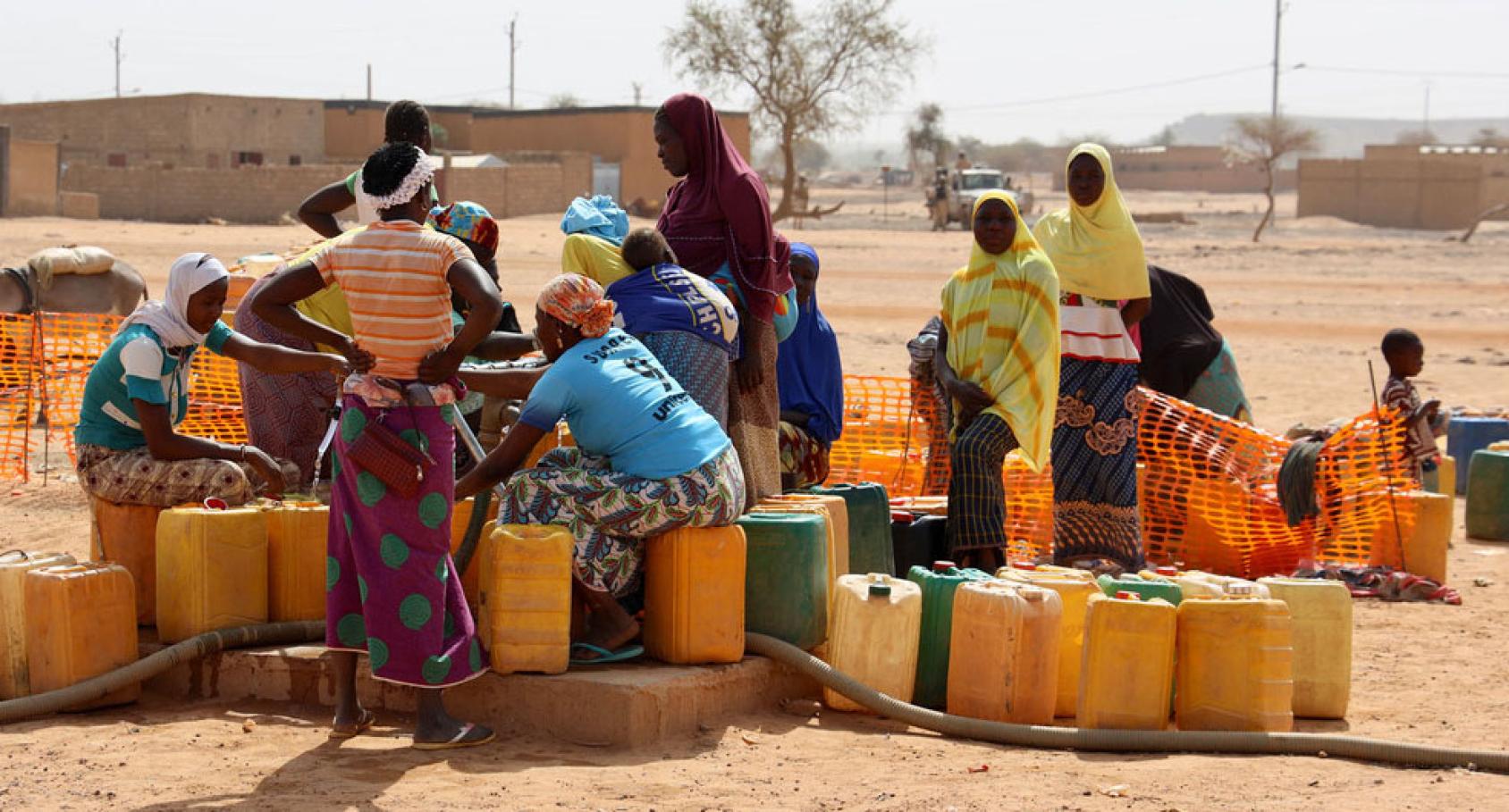 A group of women surrounded by water pitchers collect water. 