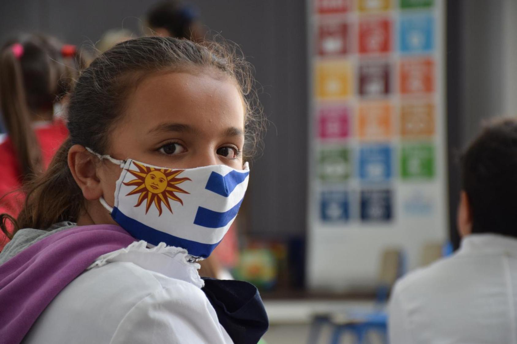 A girl looks at the camera in a face mask with Uruguay's flag.