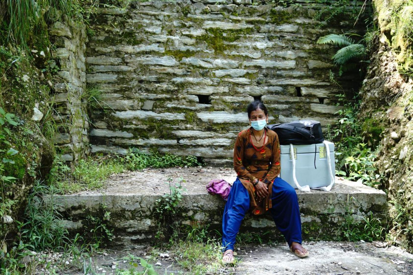 A woman rests near a rock wall with the large box next to her. 