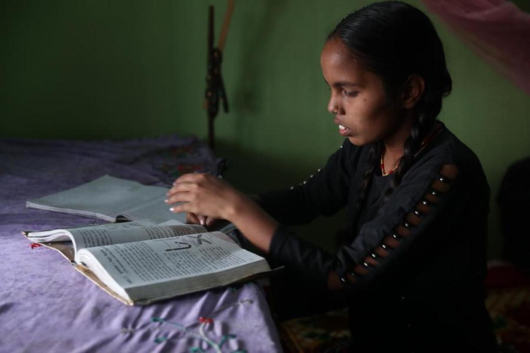 Una niña observa sus libros, los cuales están sobre una mesa con un mantel morado.