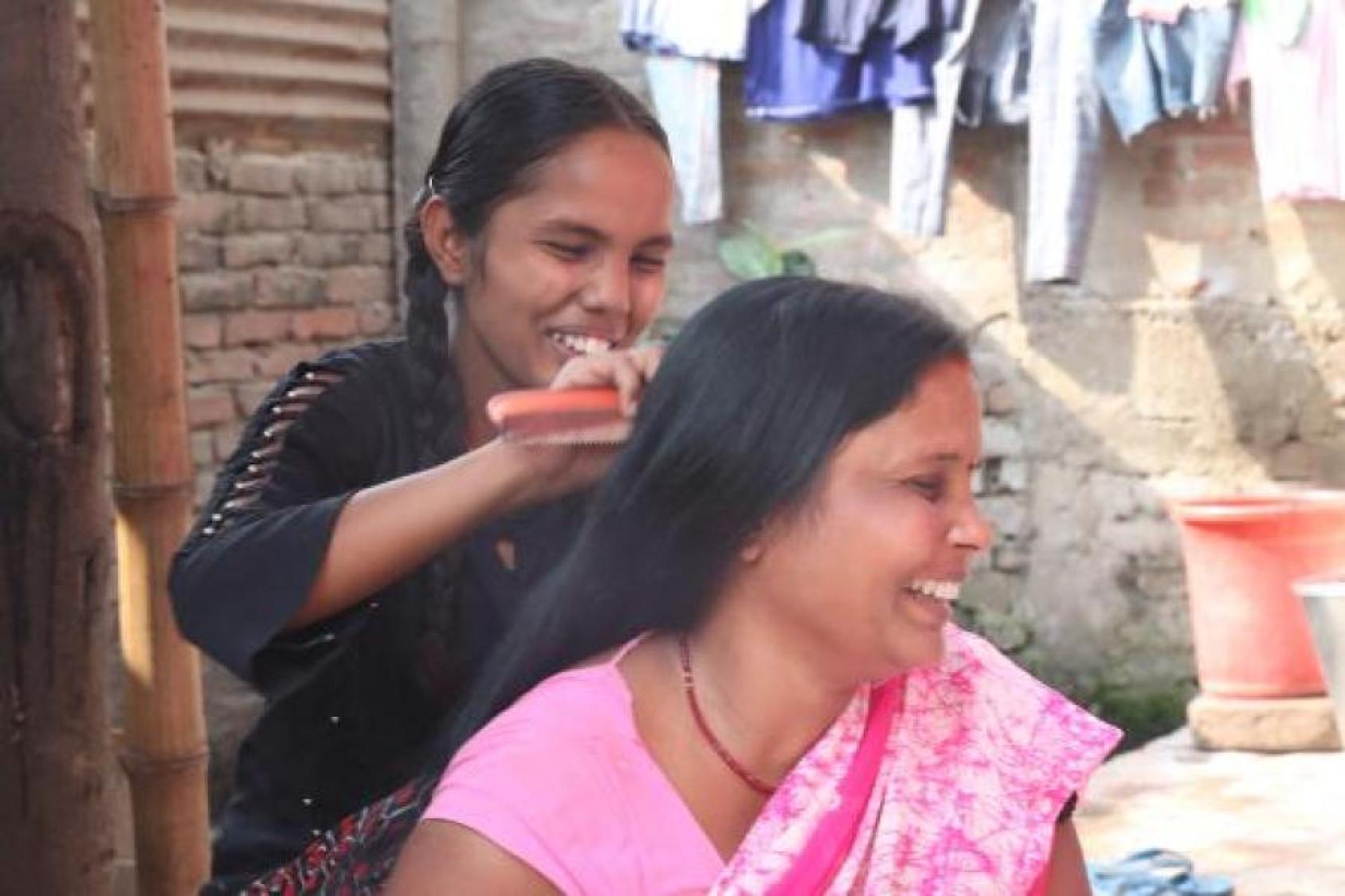 A smiling girl brushes her mother's hair.