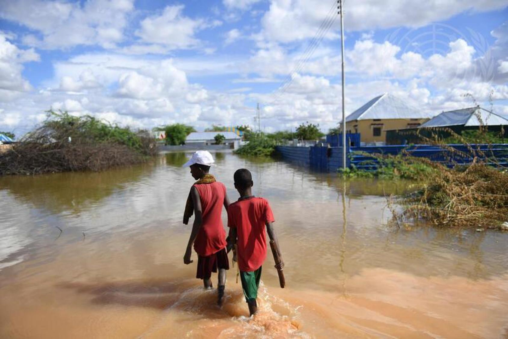 Two boys walk through a flooded area near homes.