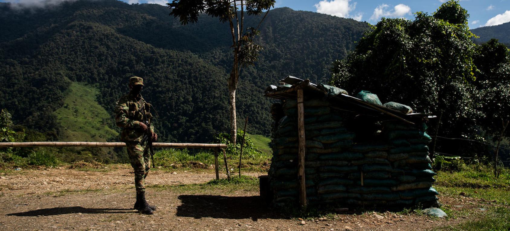 A soldier holding a weapon stands outside a small facility made of wood. 