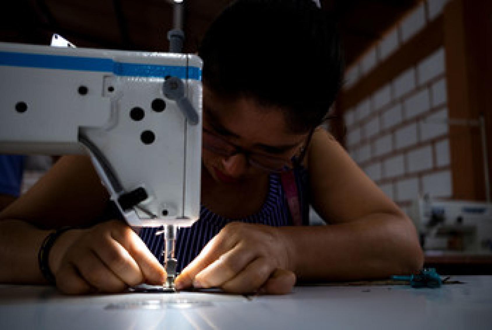 A woman closely watches as her fingers pitch the fabric she runs through the sewing machine.