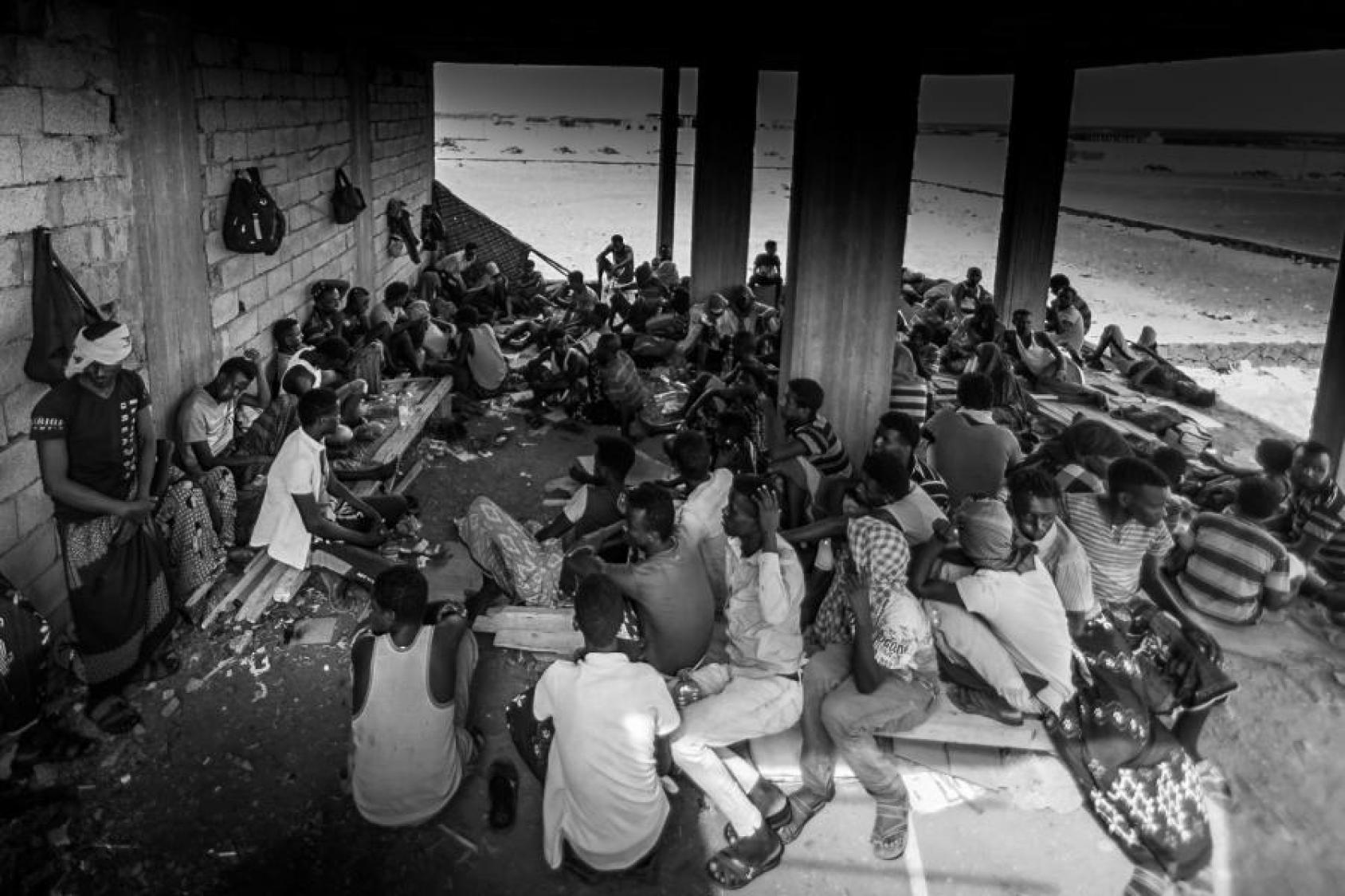A black and white image of many people all sitting closely on the ground. 