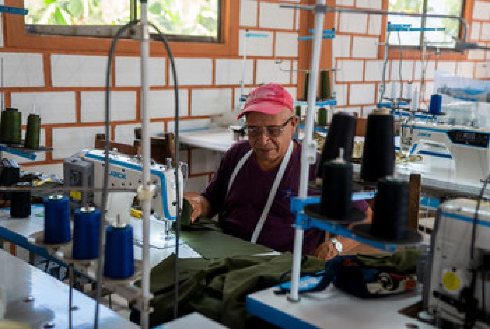 A man sits surrounded by sewing machines as he works on sewing a garment. 