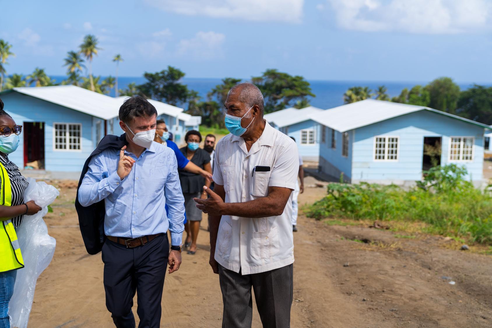 People, including the Resident Coordinator, walk through a re-built area with homes. 
